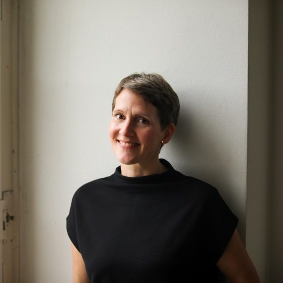 Portraitfoto von Ina Hartmann, Texterin und Autorin. Sie hat kurze Haare und ein offenes Lächeln, trägt ein schwarzes Shirt. 